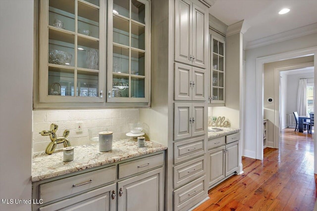 bar featuring decorative backsplash, light stone counters, crown molding, and light hardwood / wood-style flooring