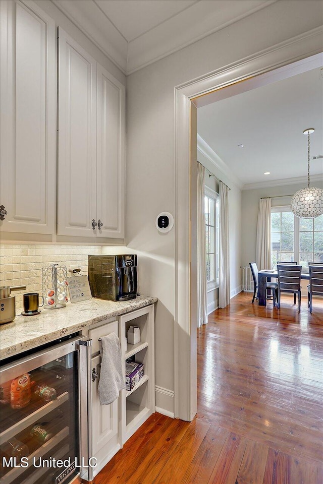 bar with tasteful backsplash, wine cooler, crown molding, wood-type flooring, and white cabinets