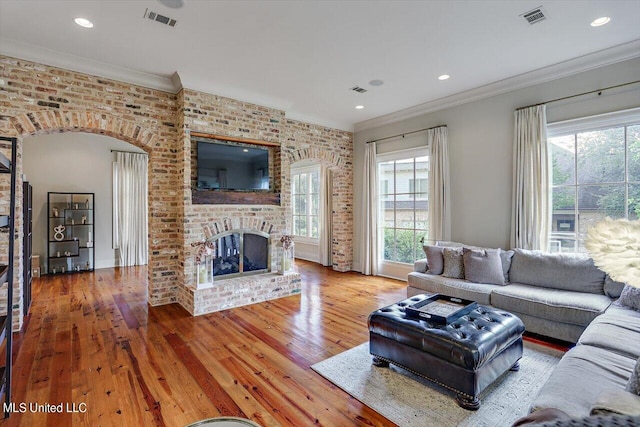 living room featuring a healthy amount of sunlight, wood-type flooring, crown molding, and a brick fireplace