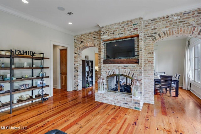 living room featuring crown molding, a fireplace, wood-type flooring, and brick wall