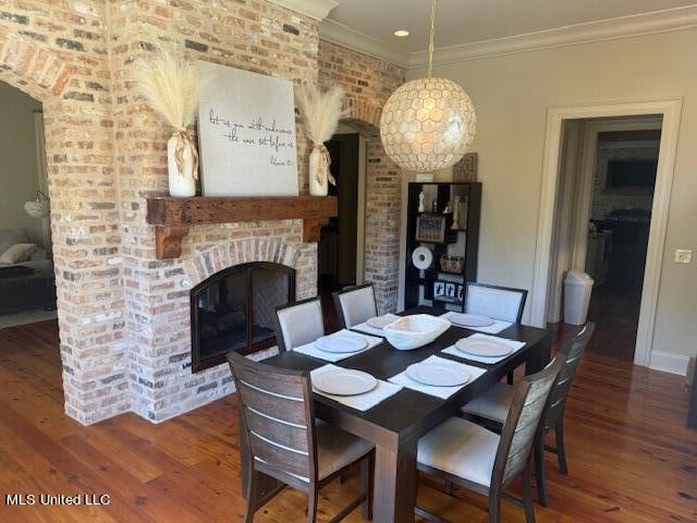 dining space with hardwood / wood-style floors, crown molding, brick wall, and a brick fireplace