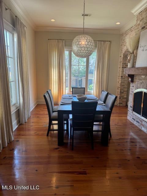 dining area with dark hardwood / wood-style floors, crown molding, and a brick fireplace