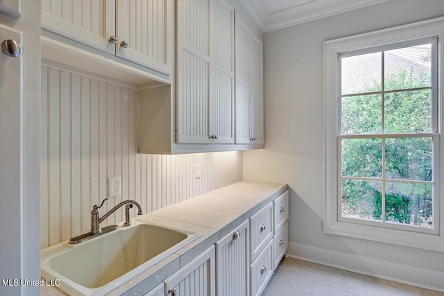 laundry area with plenty of natural light, ornamental molding, sink, and light tile patterned floors