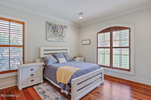 bedroom with wood-type flooring, multiple windows, and ornamental molding