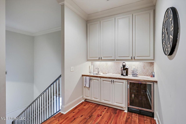 bar featuring decorative backsplash, light wood-type flooring, ornamental molding, beverage cooler, and white cabinets