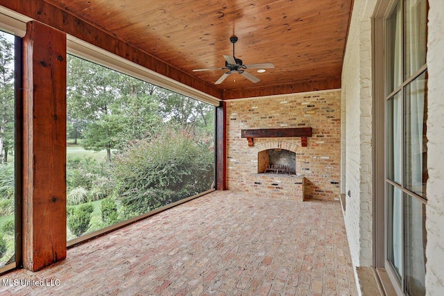 unfurnished sunroom with ceiling fan, wooden ceiling, and a brick fireplace