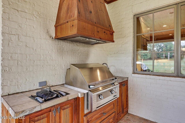 kitchen with tile counters, premium range hood, and brick wall