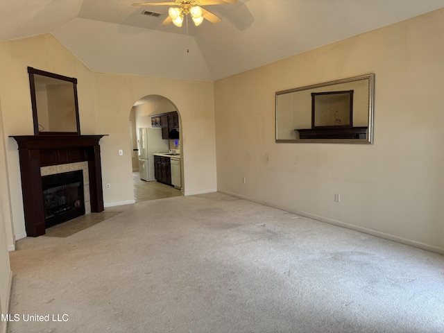 unfurnished living room with light carpet, vaulted ceiling, ceiling fan, and a tiled fireplace