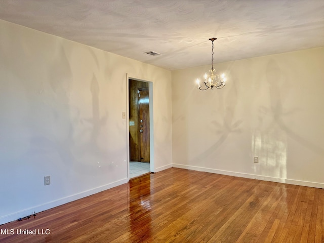 empty room featuring wood-type flooring and an inviting chandelier