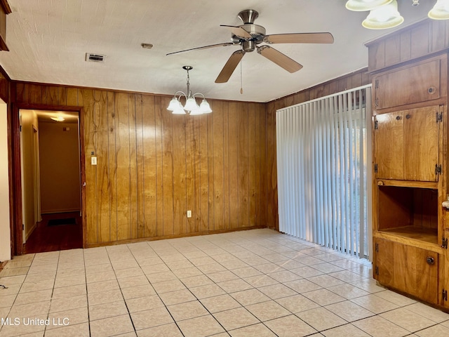 tiled spare room featuring wood walls and ceiling fan with notable chandelier