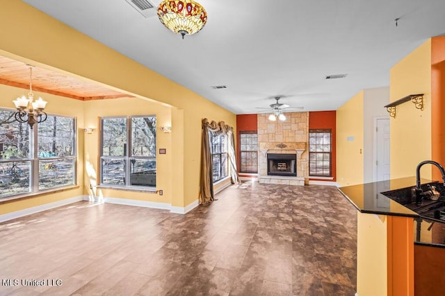 unfurnished living room featuring visible vents, ceiling fan with notable chandelier, a stone fireplace, and baseboards