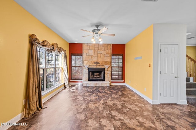 unfurnished living room featuring stairway, baseboards, a stone fireplace, and ceiling fan