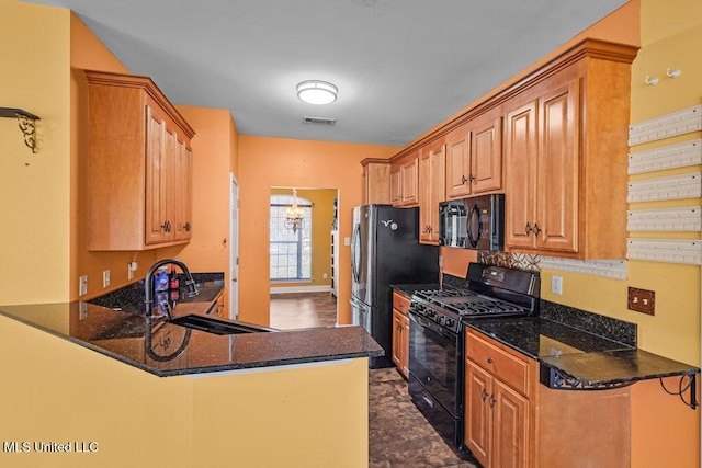 kitchen featuring visible vents, black appliances, a sink, dark stone countertops, and a peninsula