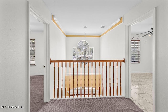 hall with visible vents, carpet flooring, crown molding, a notable chandelier, and tile patterned floors