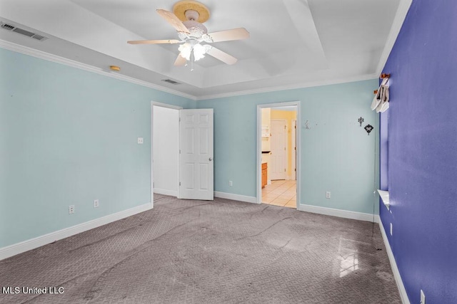 unfurnished bedroom with a tray ceiling, visible vents, ornamental molding, and carpet flooring