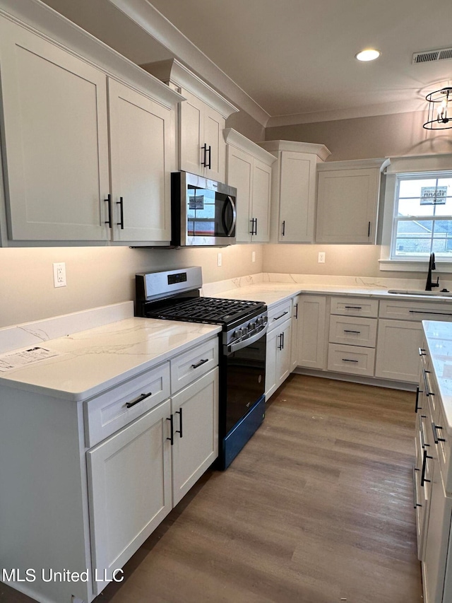 kitchen with sink, black gas stove, hardwood / wood-style floors, white cabinets, and crown molding