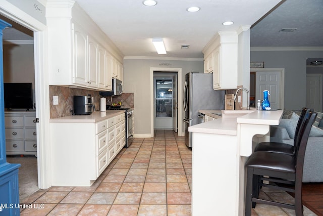 kitchen featuring a breakfast bar area, stainless steel appliances, a peninsula, decorative columns, and crown molding