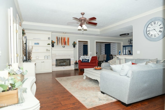 living area with dark wood-type flooring, a glass covered fireplace, ornamental molding, and ceiling fan