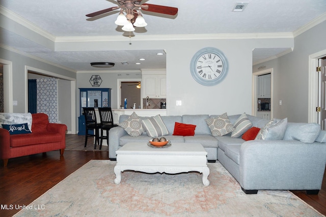 living room with ornamental molding, wood finished floors, visible vents, and a ceiling fan