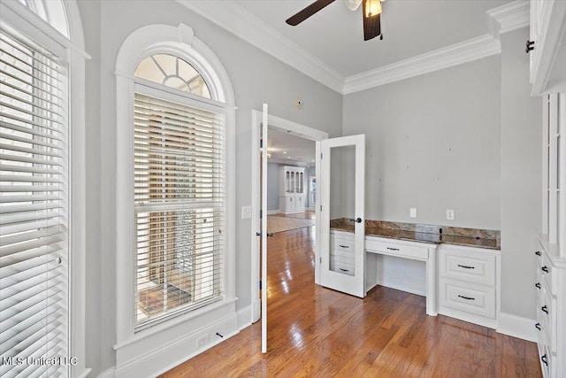 unfurnished office featuring built in desk, ornamental molding, hardwood / wood-style floors, and ceiling fan