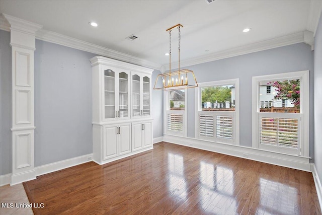 unfurnished dining area featuring dark wood-type flooring, ornate columns, and ornamental molding