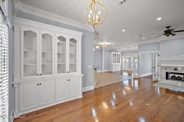 dining room with ornamental molding, a fireplace, wood-type flooring, and ceiling fan with notable chandelier