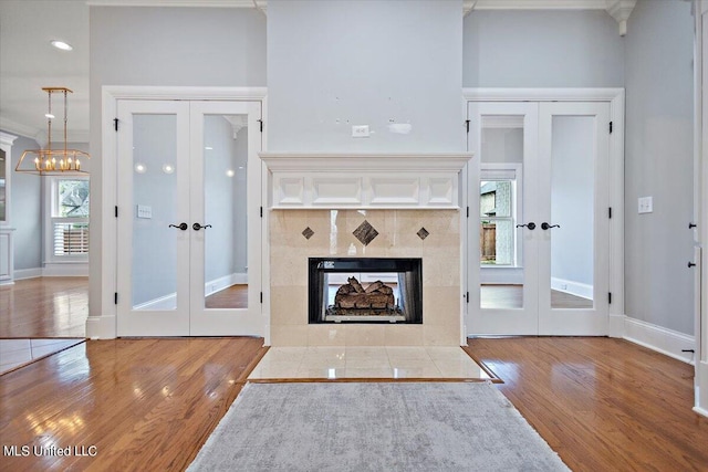 unfurnished living room with ornamental molding, french doors, hardwood / wood-style floors, and a tiled fireplace