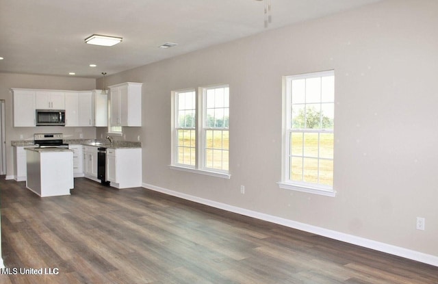 kitchen with baseboards, dark wood-type flooring, white cabinetry, a kitchen island, and stainless steel appliances