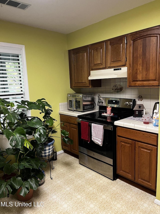 11423 High Rd, Hernando, MS 38632 - kitchen with stainless steel range with electric stovetop, under cabinet range hood, tile counters, decorative backsplash, and dark brown cabinets