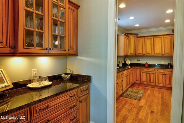 kitchen featuring ornamental molding, light wood-type flooring, and dark stone counters