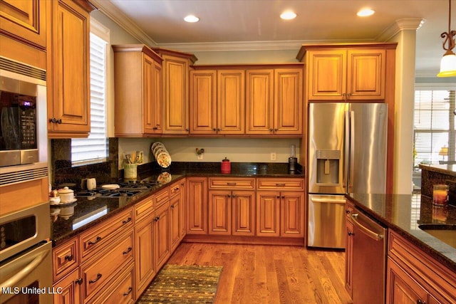 kitchen featuring hanging light fixtures, dark stone countertops, ornamental molding, light wood-type flooring, and appliances with stainless steel finishes