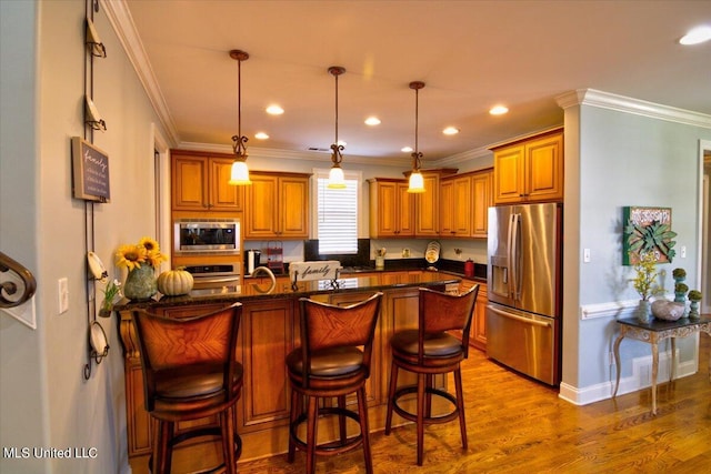 kitchen featuring a kitchen bar, light hardwood / wood-style flooring, pendant lighting, crown molding, and stainless steel appliances