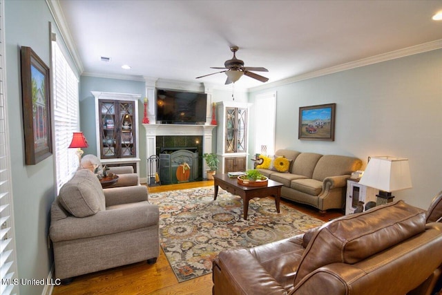 living room featuring crown molding, wood-type flooring, a tile fireplace, and ceiling fan