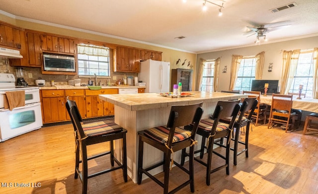 kitchen featuring backsplash, light wood-type flooring, ornamental molding, sink, and white appliances