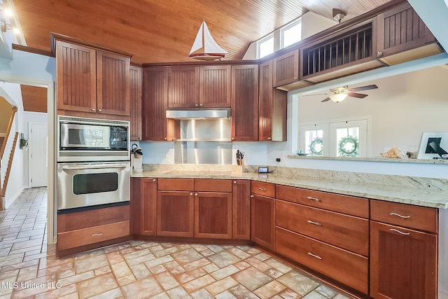 kitchen featuring light stone counters, oven, under cabinet range hood, vaulted ceiling, and built in microwave