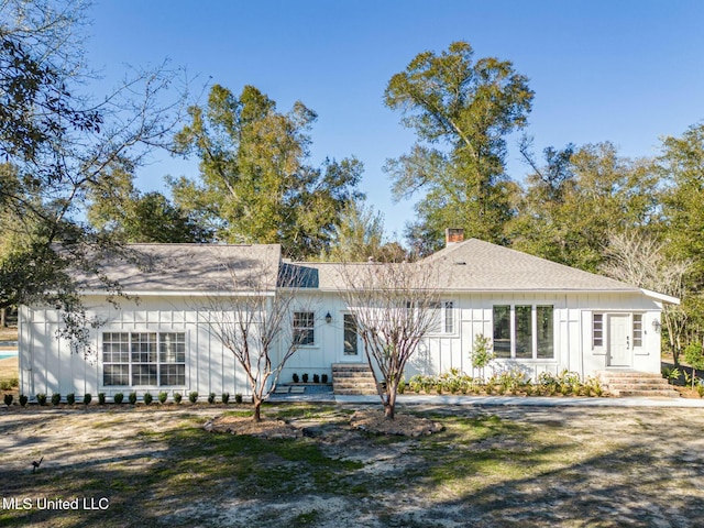 single story home with entry steps, a shingled roof, a chimney, and board and batten siding