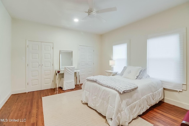 bedroom featuring wood finished floors, two closets, a ceiling fan, and baseboards