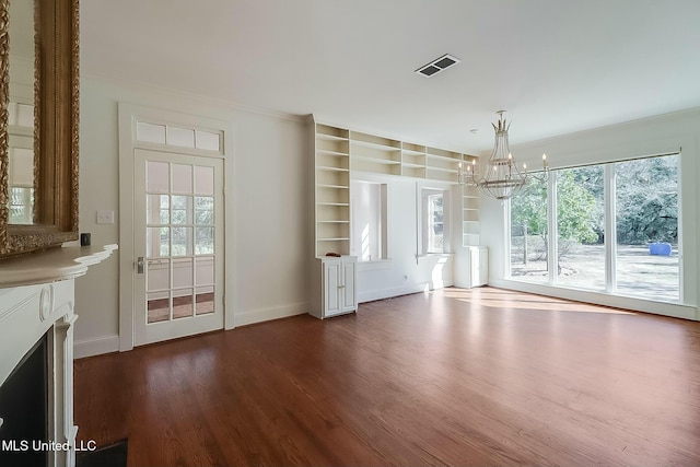 unfurnished living room featuring dark wood-style flooring, plenty of natural light, visible vents, and an inviting chandelier