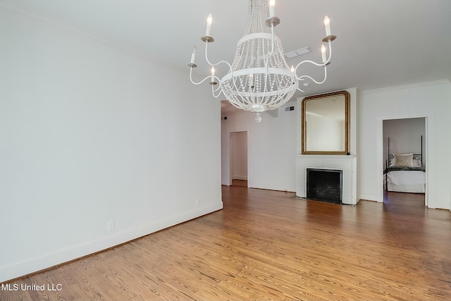 unfurnished living room with a large fireplace, baseboards, ornamental molding, wood finished floors, and a chandelier