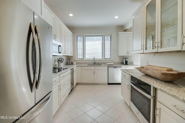 kitchen with light stone counters, recessed lighting, a sink, appliances with stainless steel finishes, and glass insert cabinets