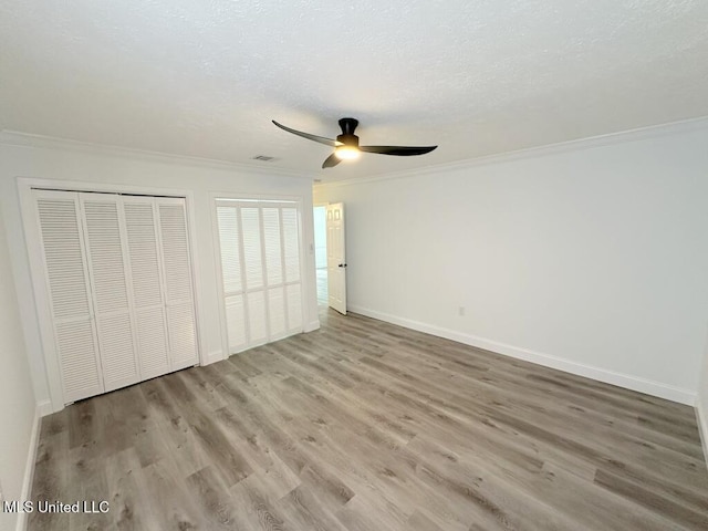 unfurnished bedroom featuring a textured ceiling, crown molding, baseboards, and wood finished floors