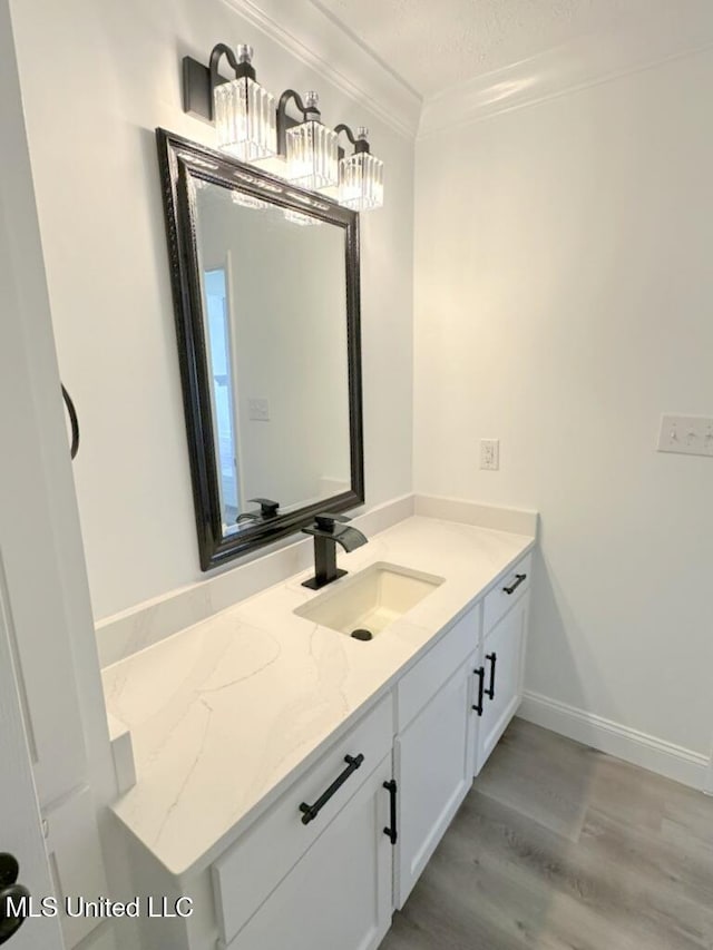 bathroom with vanity, crown molding, wood finished floors, and baseboards