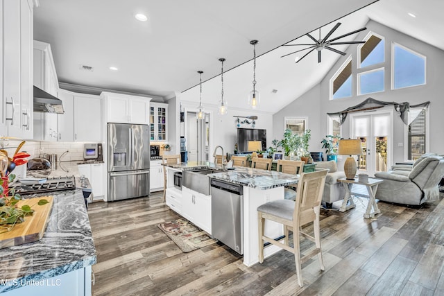 kitchen featuring dark stone countertops, appliances with stainless steel finishes, range hood, white cabinets, and a kitchen island with sink