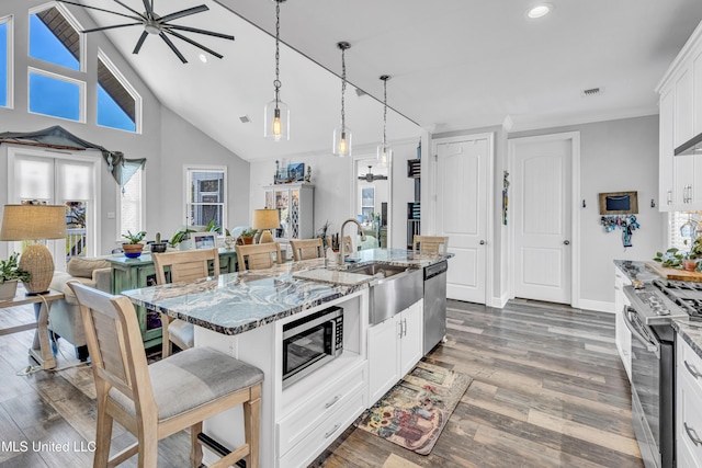 kitchen featuring a center island with sink, light stone countertops, appliances with stainless steel finishes, white cabinets, and a kitchen breakfast bar