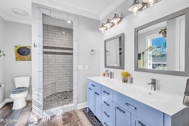 bathroom with toilet, a tile shower, hardwood / wood-style floors, ornamental molding, and vanity