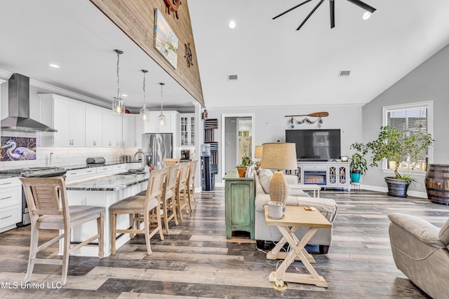 interior space featuring a center island with sink, appliances with stainless steel finishes, decorative light fixtures, wall chimney range hood, and a breakfast bar area