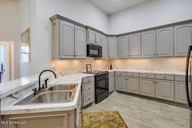 kitchen with a high ceiling, black appliances, sink, light hardwood / wood-style flooring, and kitchen peninsula