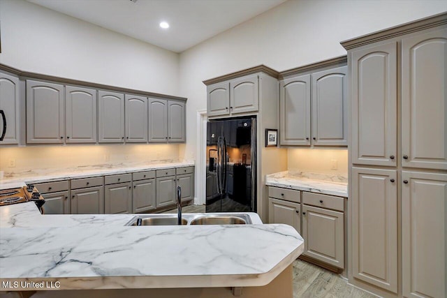 kitchen featuring gray cabinetry, black fridge with ice dispenser, sink, and light hardwood / wood-style flooring