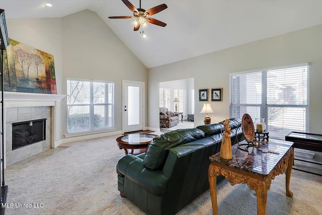 living room with a tiled fireplace, ceiling fan, high vaulted ceiling, and light colored carpet