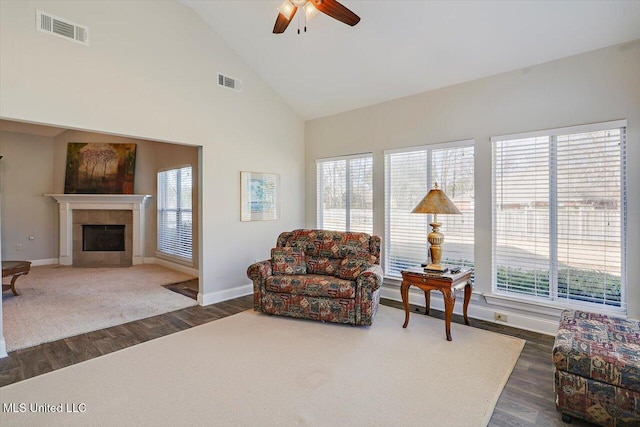 living room with ceiling fan, dark wood-type flooring, a tile fireplace, and vaulted ceiling